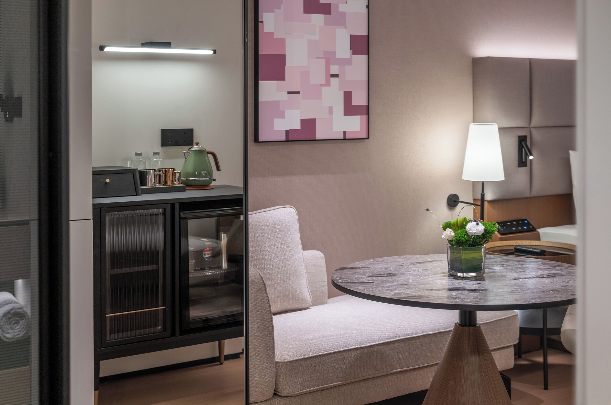 A modern room with a sofa, a round table with a vase, a lamp, and a cabinet with glass doors.
