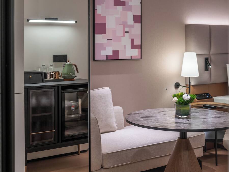 A modern room with a sofa, a round table with a vase, a lamp, and a cabinet with glass doors.