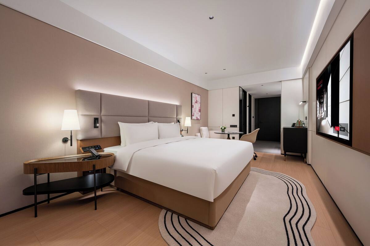 A modern hotel room with a large bed, bedside tables, a desk, and a chair.