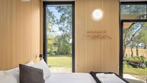 A modern bedroom with a bed, a massage table, wooden walls, and a view of the outdoors.