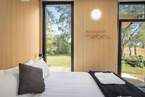 A modern bedroom with a bed, a massage table, wooden walls, and a view of the outdoors.