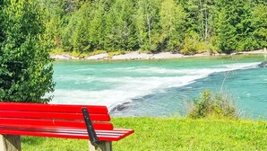 Eine rote Bank am Flussufer, mit einem Wald im Hintergrund.
