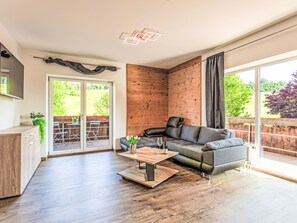 Un salon moderne avec un canapé gris, un plancher en bois, un mur décoratif en bois, une porte-fenêtre coulissante donnant sur un espace extérieur et un téléviseur à écran plat fixé au mur.