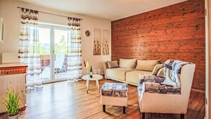 Ein gemütliches Wohnzimmer mit einer Holzvertäfelung, einer Couch, einem gemusterten Sessel, einem Couchtisch und Blick durch eine Glastür.