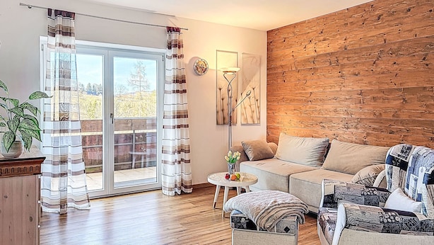 Ein Wohnzimmer mit einer Holzwand, einem Sofa, einem Couchtisch und Blick durch eine Glastür.