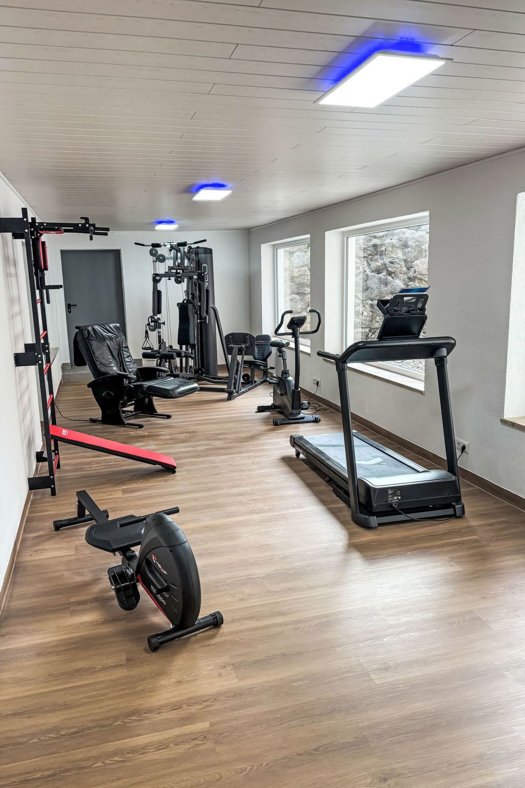 Ett gym med konditionsmaskiner, utrustning för styrketräning och en röd bänk.