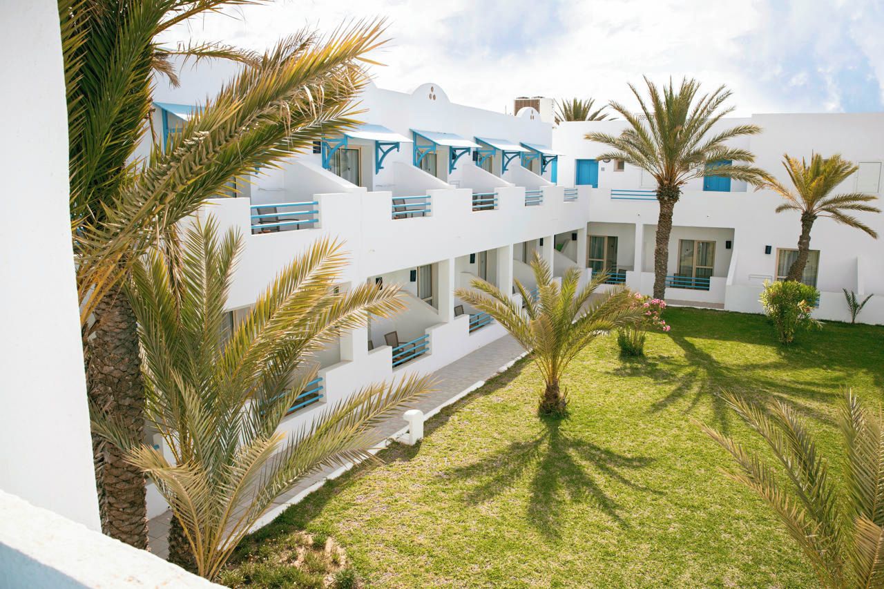 A hotel with multiple balconies, palm trees, and a well-maintained lawn.
