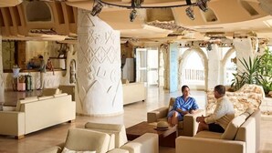 A spacious lobby with multiple seating areas, a reception desk, and a large pillar with intricate patterns. - Robinson Djerba Bahiya (Aghir)