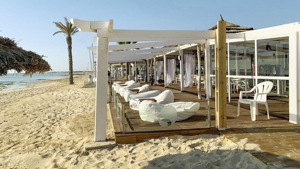 A beachside lounge with white chairs and a wooden deck, overlooking the sea. - Robinson Djerba Bahiya (Aghir)