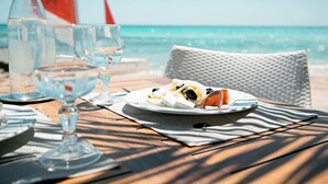 A table with a plate of food and glasses of water, set on a wooden deck with a view of the ocean. - Robinson Djerba Bahiya (Aghir)
