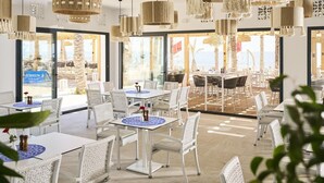A spacious outdoor dining area with white wicker furniture, hanging woven light fixtures, and large windows offering views of the beach. - Robinson Djerba Bahiya (Aghir)
