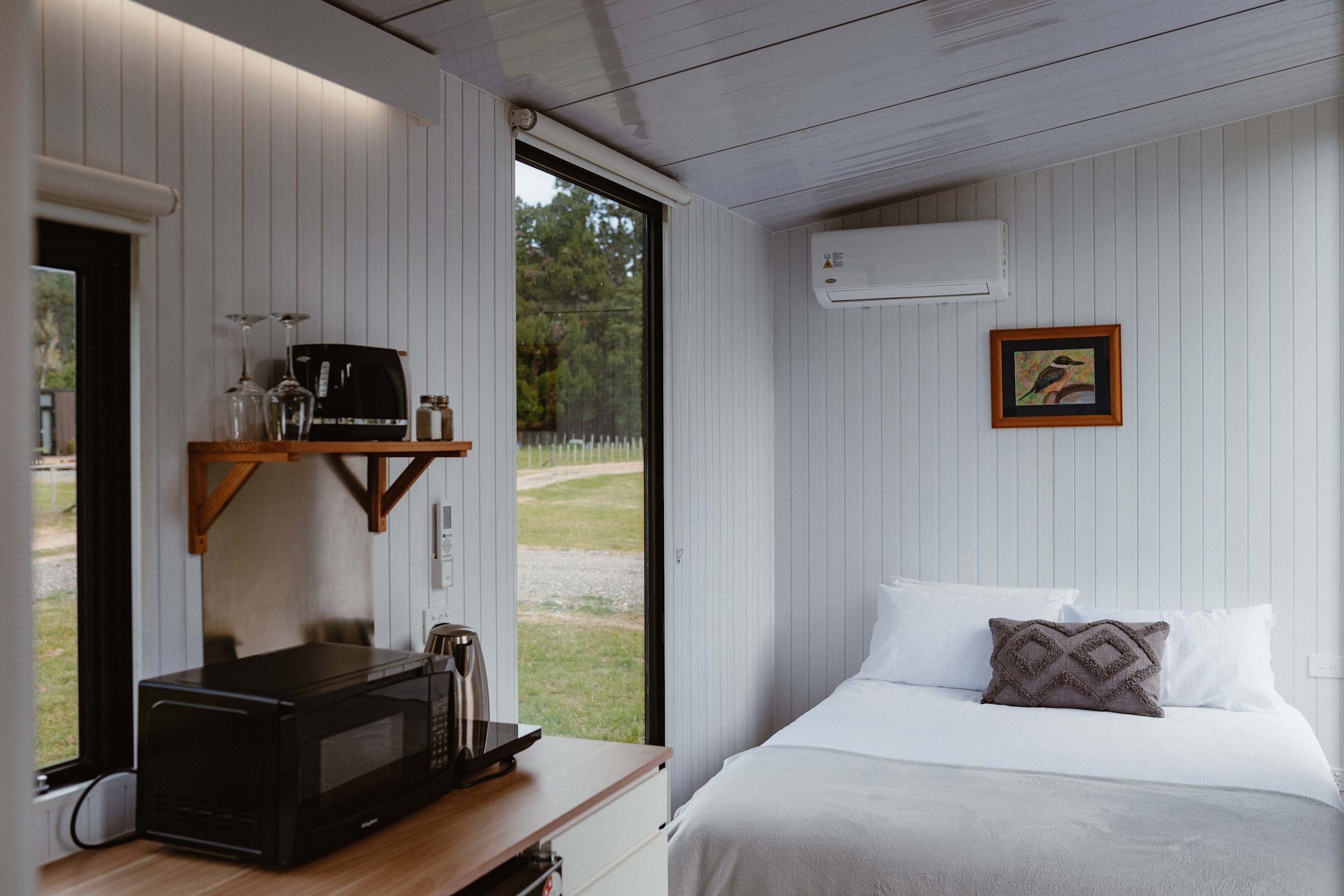 A bedroom with a bed, pillows, a coffee machine, and a window.