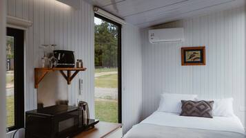 A bedroom with a bed, pillows, a coffee machine, and a window.