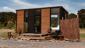 A modern cabin with a wooden exterior, large windows, a deck, and a barbecue area. - Omoho Stream X by Tiny Away (Kennedy Bay)