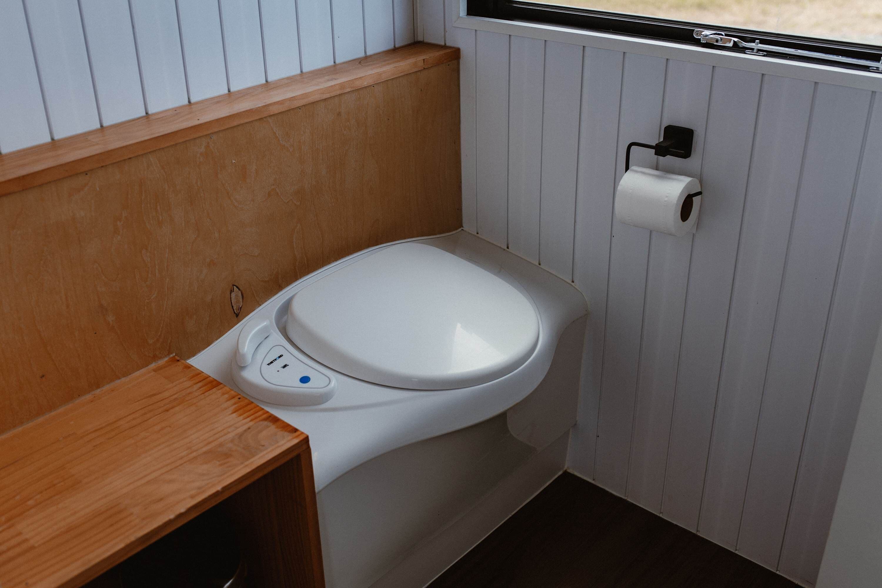 A modern bathroom with a white toilet, wooden vanity, and a window.