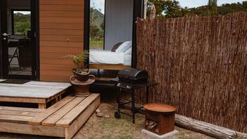 A wooden deck with a grill, a small table, and a seating area with a view of a bedroom.