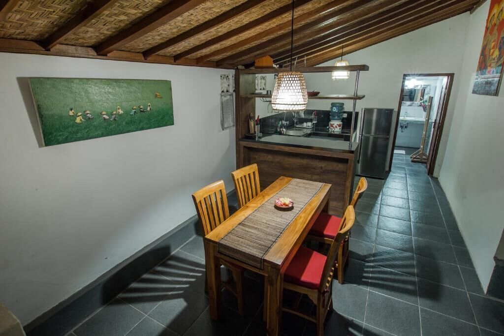 Een eetruimte met een houten tafel en stoelen, een groen schilderij aan de muur en een keuken op de achtergrond.