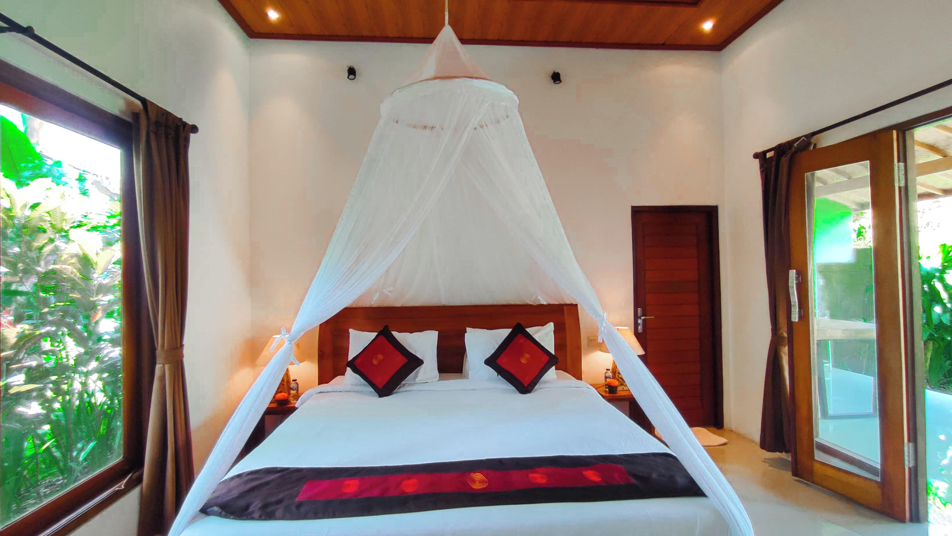 A bedroom with a canopy bed, a wooden ceiling, and a sliding glass door leading to a balcony.