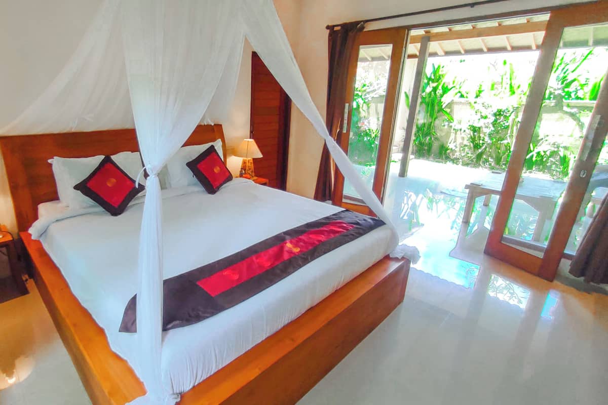 A bed with a canopy, a nightstand with a lamp, and a view of a garden through a glass door.