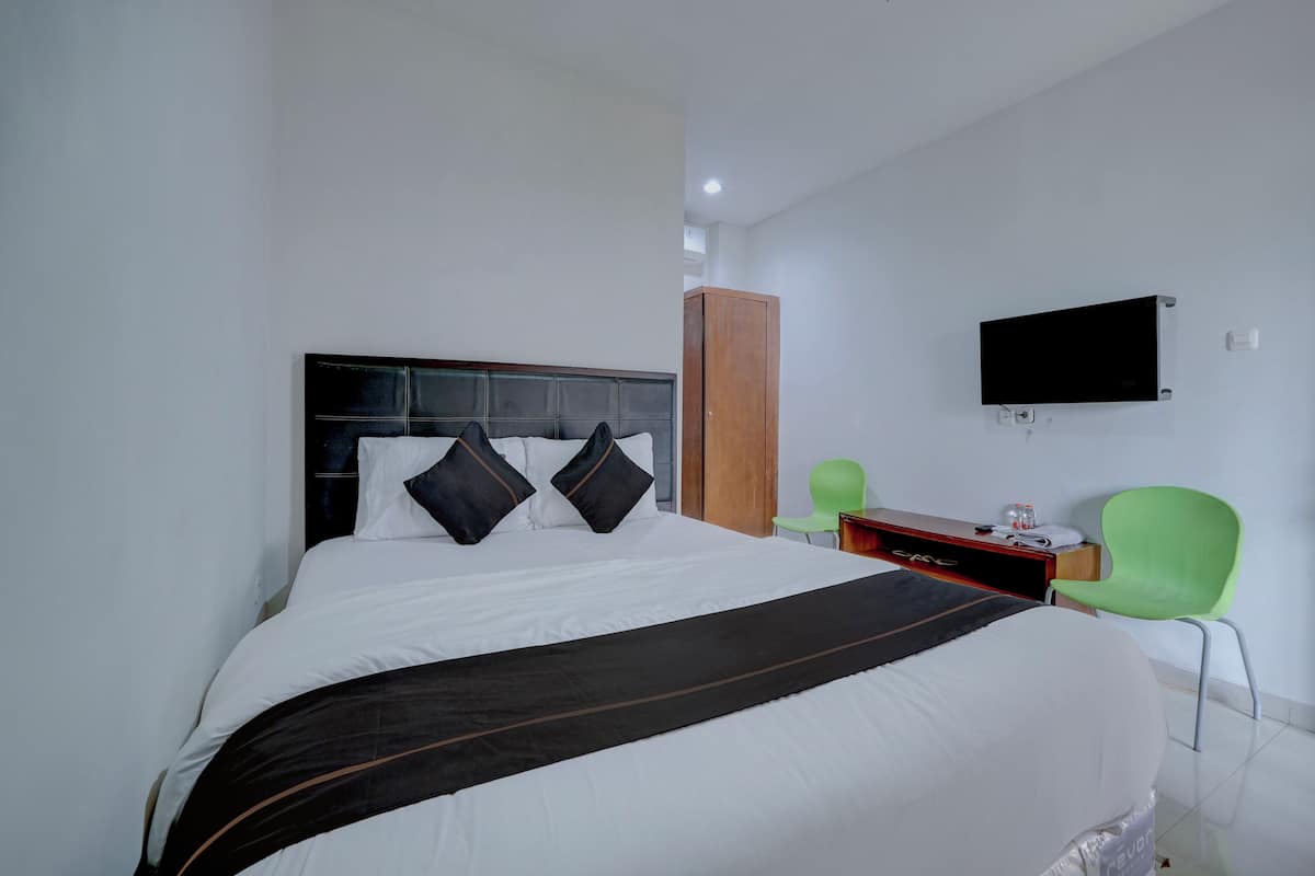 Ein Hotelzimmer mit Bett, Wandfernseher, grünem Sessel und Holzschrank.
