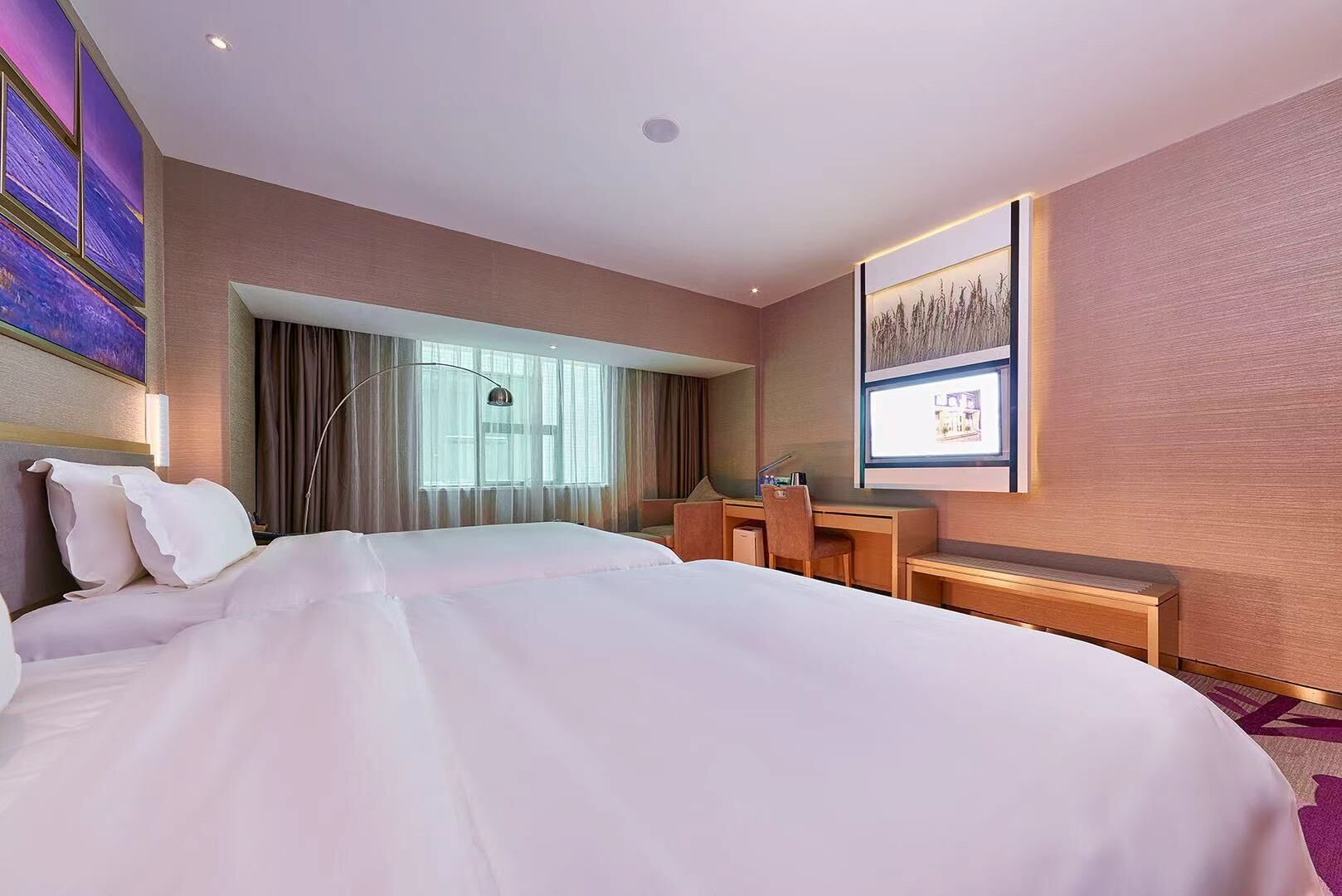 Une chambre d’hôtel avec un grand lit, un bureau et une chaise. Il y a une fenêtre avec des rideaux et un tableau au mur.