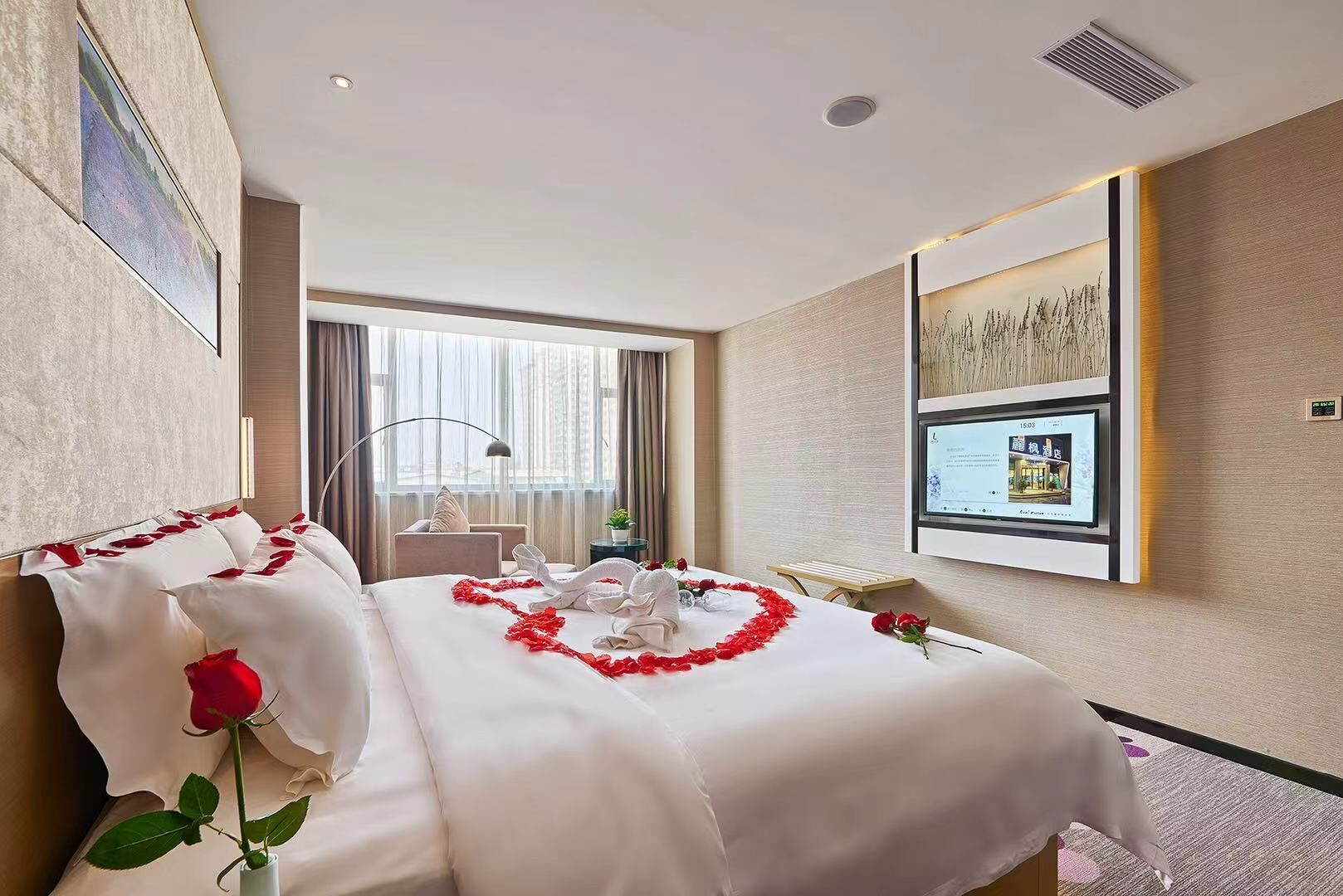 A hotel room with a large bed, a desk, a chair, a TV, and a window with curtains.