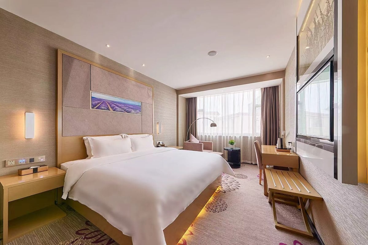 A modern hotel room with a large bed, bedside tables, a desk, and a chair.