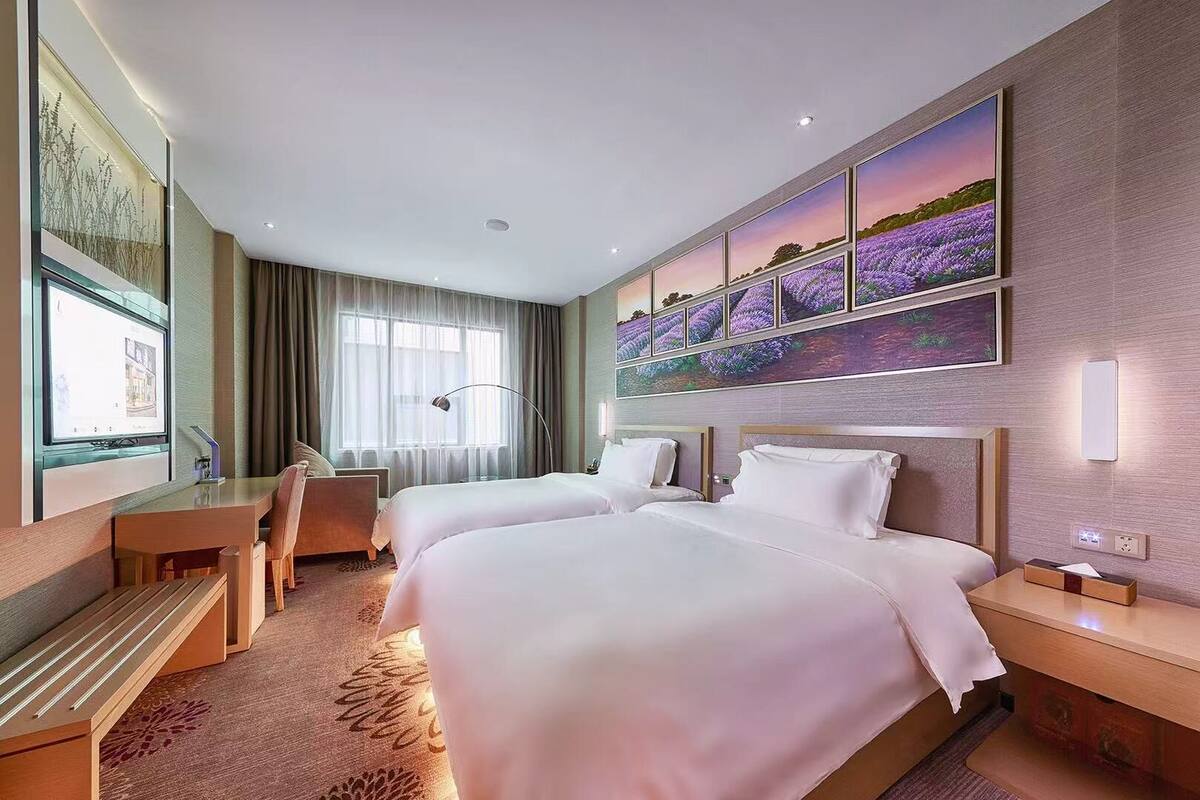 A hotel room with two beds, a desk, a chair, a TV, and a large window with curtains.