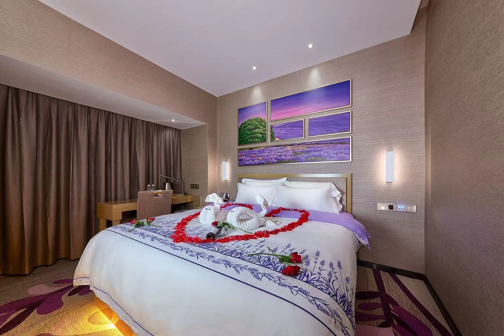 A hotel room with a large bed, a desk, a chair, and a painting of a sunset over a field.
