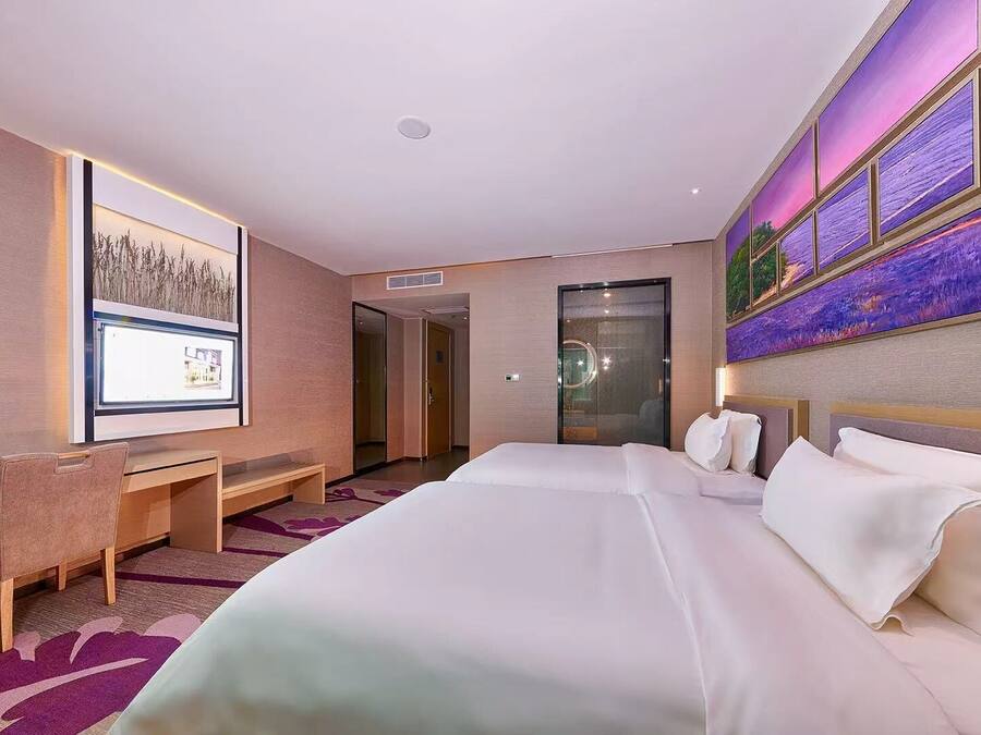 A hotel room with a large bed, a desk with a chair, a television, and a painting on the wall.