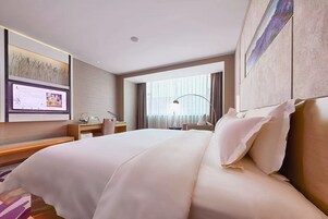Habitación de hotel con una cama grande, un escritorio, una silla, un televisor y una ventana con cortinas.