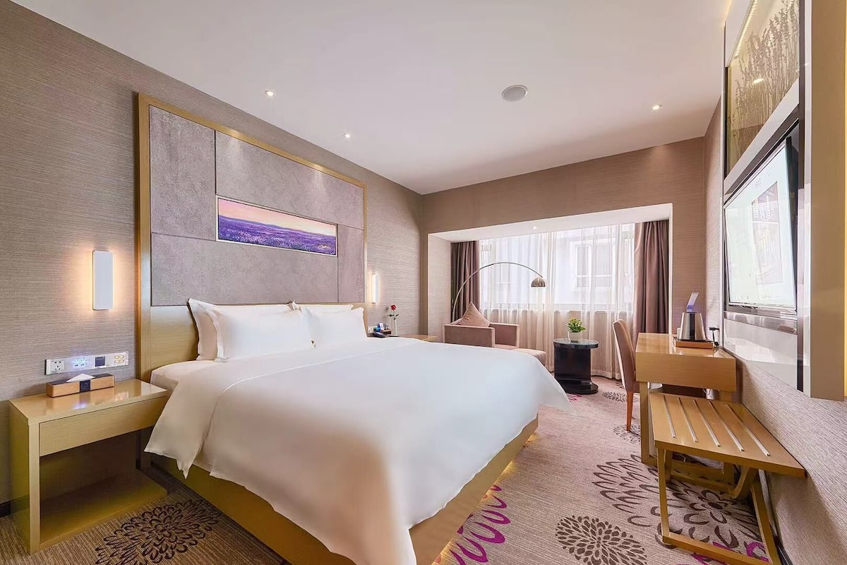 A hotel room with a large bed, bedside tables, a desk, and a chair.