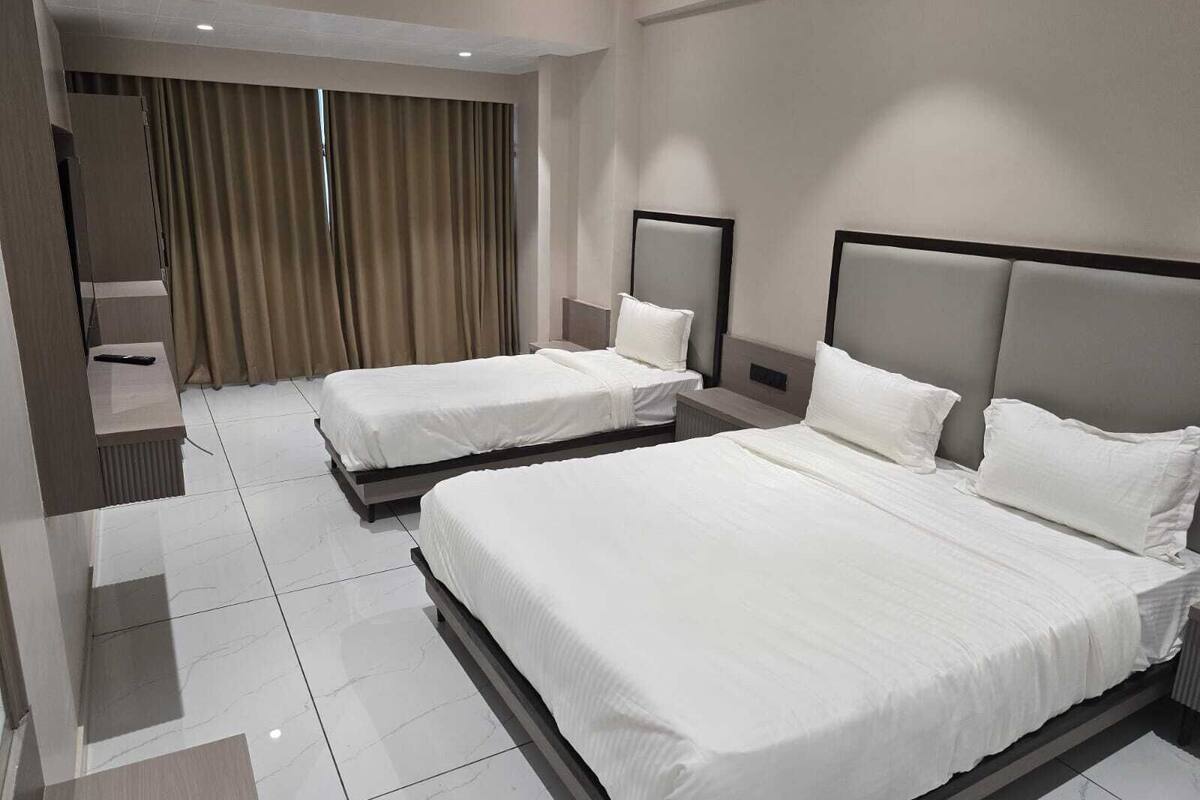 A hotel room with two beds, a large window with curtains, a ceiling fan, and a built-in TV.