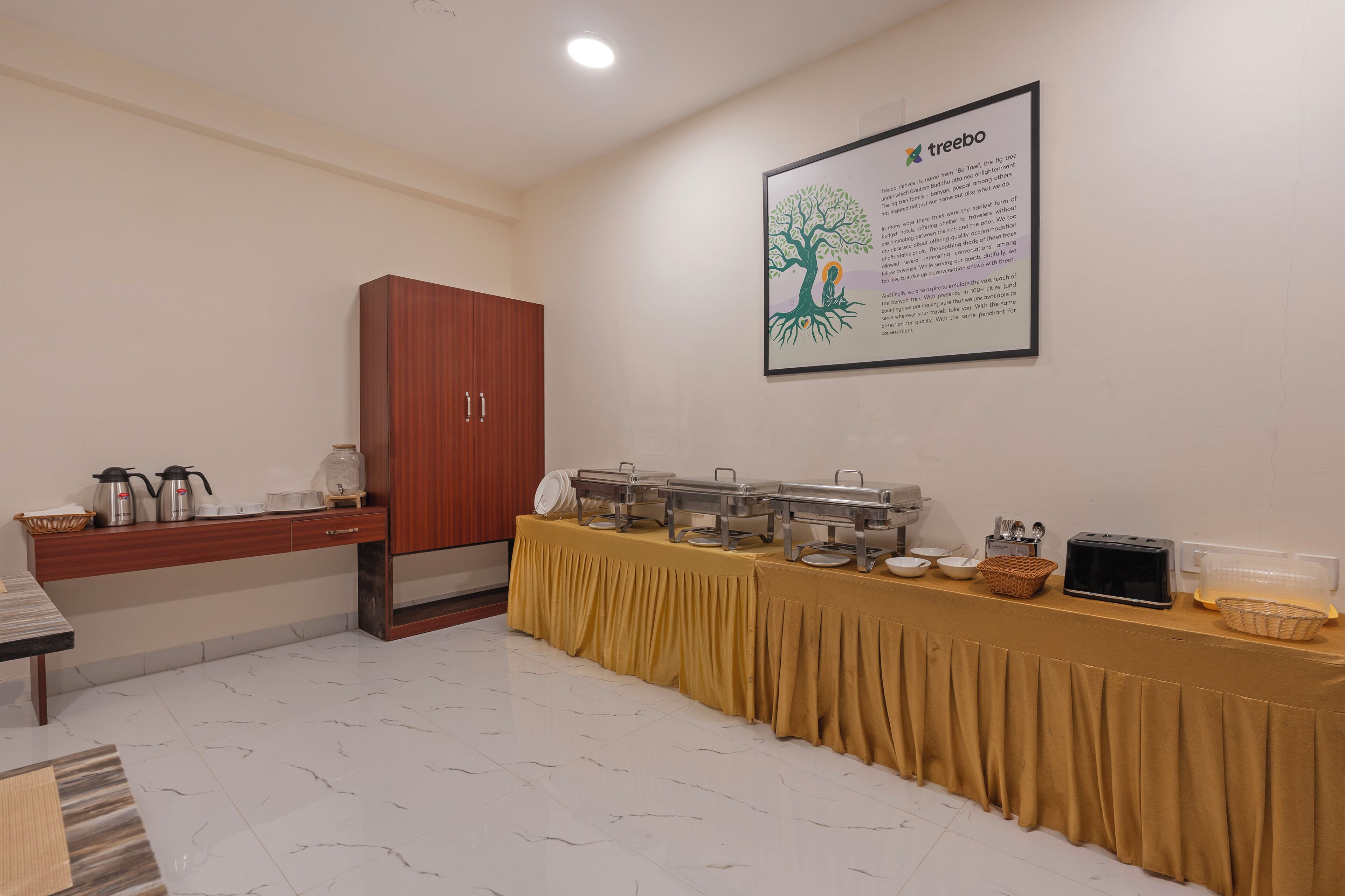 Montaje de bufé con una mesa cubierta con tela amarilla, un mueble de madera y un cartel informativo enmarcado en la pared.