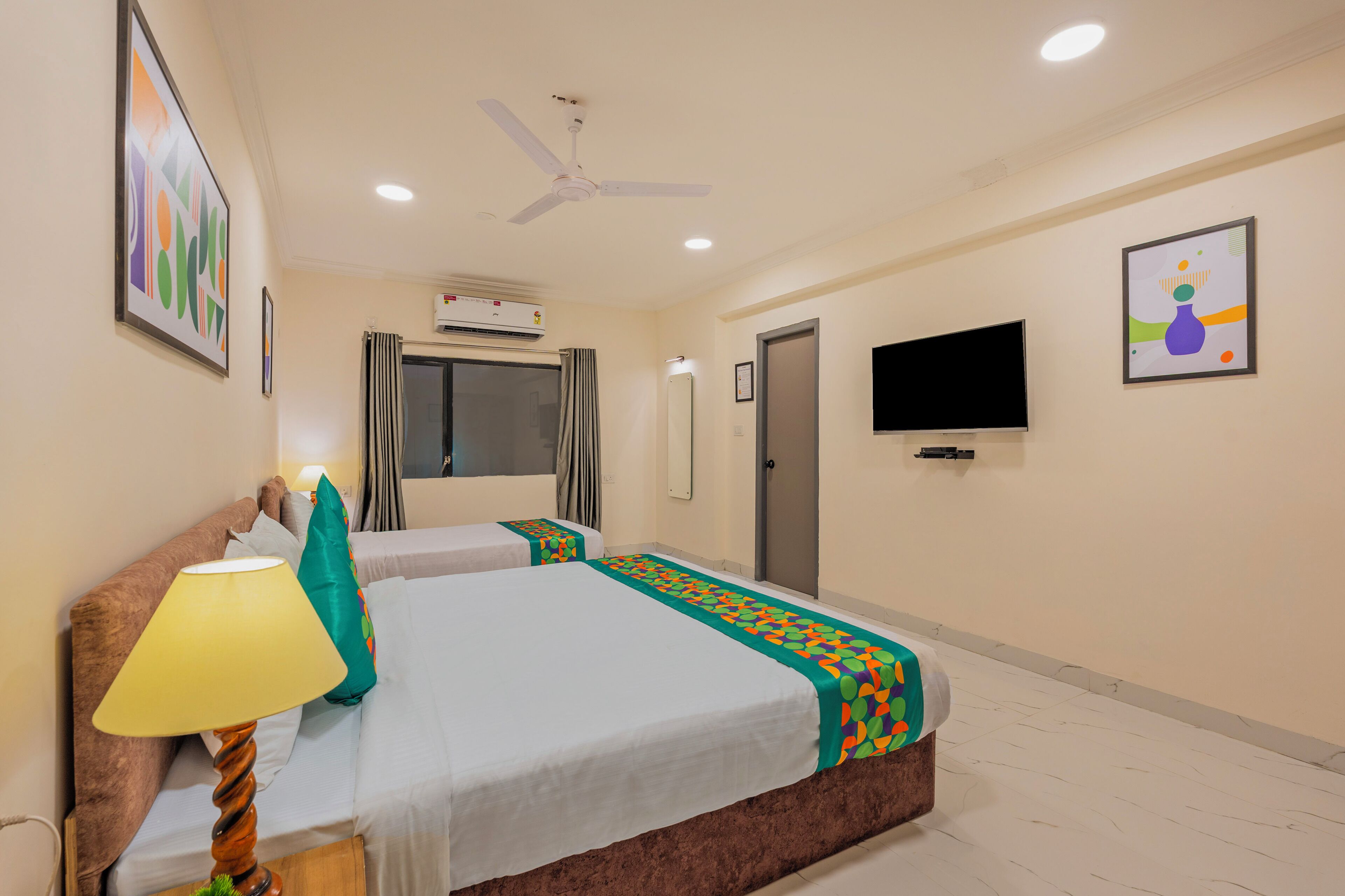 A hotel room with two beds, a ceiling fan, a TV, and an air conditioning unit.