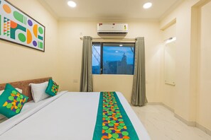 A hotel room with a bed, a window with curtains, an air conditioning unit, and a wall-mounted artwork. - Treebo GT Meridian, T-Nagar (Chennai)