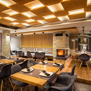 A modern dining area with wooden tables, grey upholstered chairs, and a stone fireplace. - 6ato Hotel Sofia (Sofia)