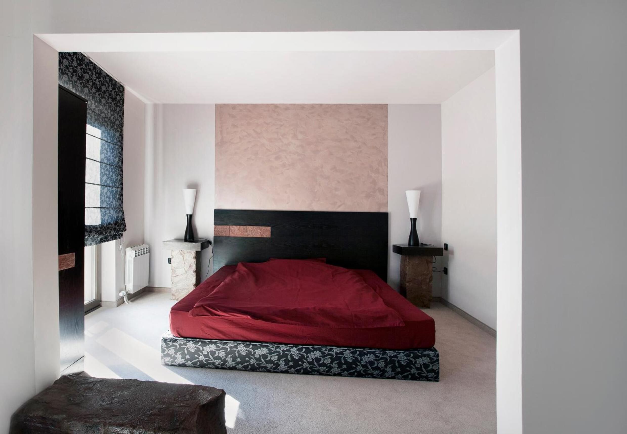 A bedroom with a bed, two bedside tables, a window, and a radiator.