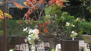 An outdoor dining area with a table set for two, featuring a bottle of wine, a vase with flowers, and a plate of food. - 6ato Hotel Sofia (Sofia)