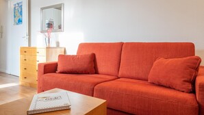 Ett rum med en röd soffa, en byrå i trä, en spegel och en karta på väggen.