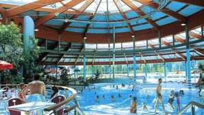 En inomhuspool med högt tak och glasväggar, omgiven av metallräcken och stolar.
