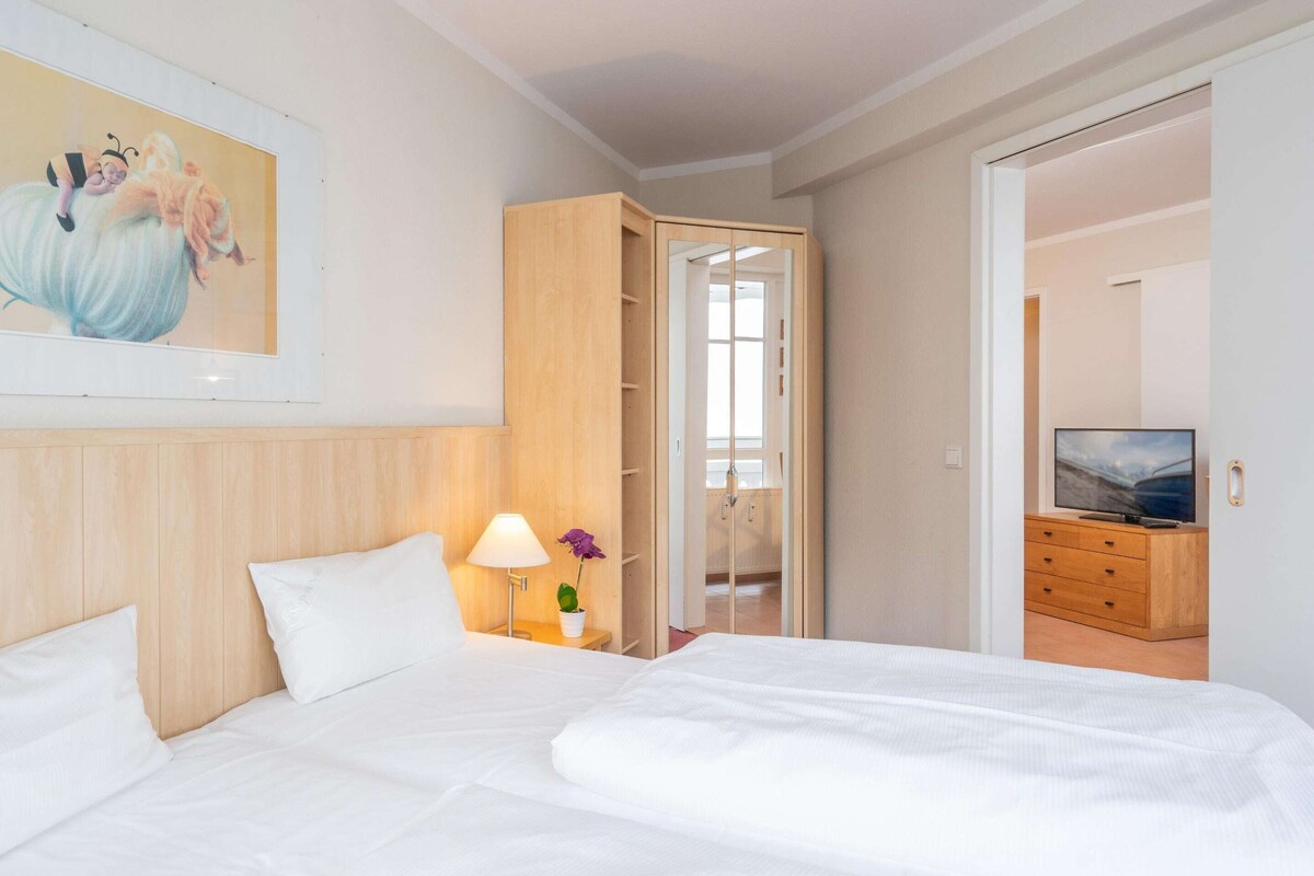 Ein Hotelzimmer mit Bett, Nachttisch mit Lampe, Fernseher, Holzschrank und angrenzendem Badezimmer.
