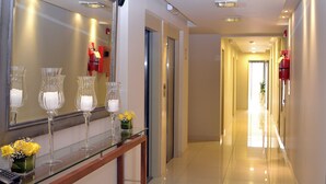 A hotel corridor with a reflective wall, a glass display case with candles, and a door leading to another room. - Kube Apartment Express (Córdoba)