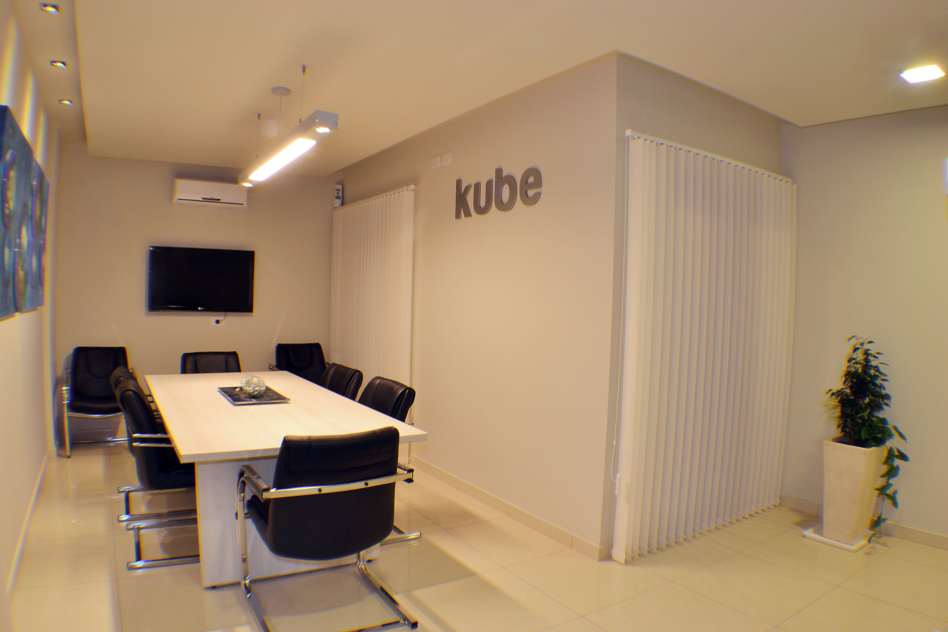 A conference room with a long table, chairs, a flat-screen TV, and a 'kube' sign on the wall.