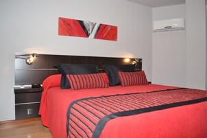 Un dormitorio moderno con una cama grande, mesitas de noche, aire acondicionado instalado en la pared y un cuadro abstracto rojo.