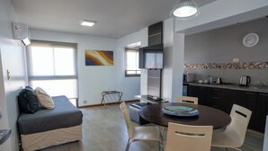 A modern kitchen with a microwave, toaster, and kettle, a dining table with chairs, a sofa with cushions, and a large window. - Kube Apartment Express (Córdoba)