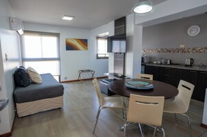 Una cocina moderna con microondas, tostadora y hervidor, una mesa de comedor con sillas, un sofá con cojines y un ventanal grande.