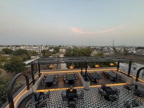 An outdoor seating area with tables and chairs, a patterned floor, and a view of a cityscape in the background. - Hotel Annant Jawai (Sumerpur)