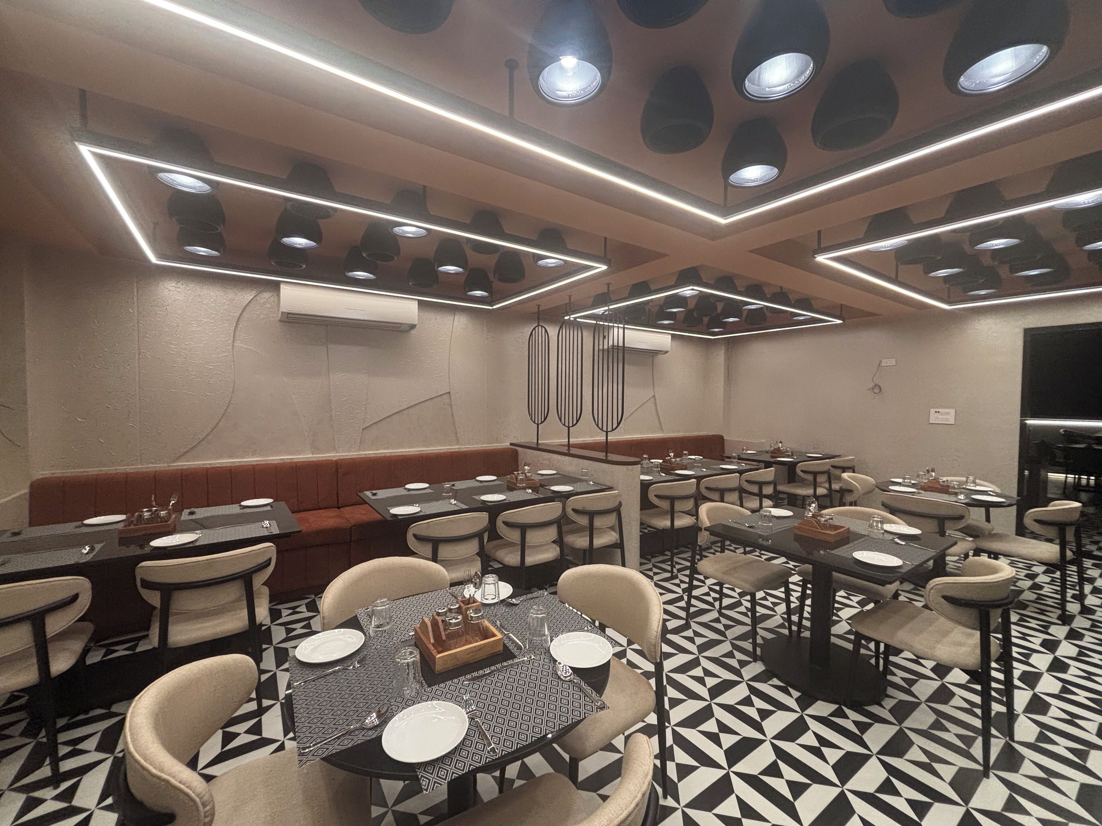A restaurant with multiple tables and booths, geometric patterned flooring, and modern lighting fixtures.