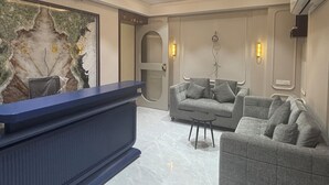 Una moderna zona de recepción con una pared de mármol, un mostrador de recepción y un área de estar con sofás y una pequeña mesa.